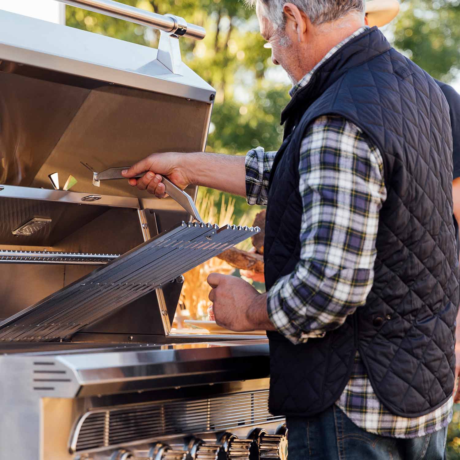 Person grilling with the dual fuel grill lid open over hot grates