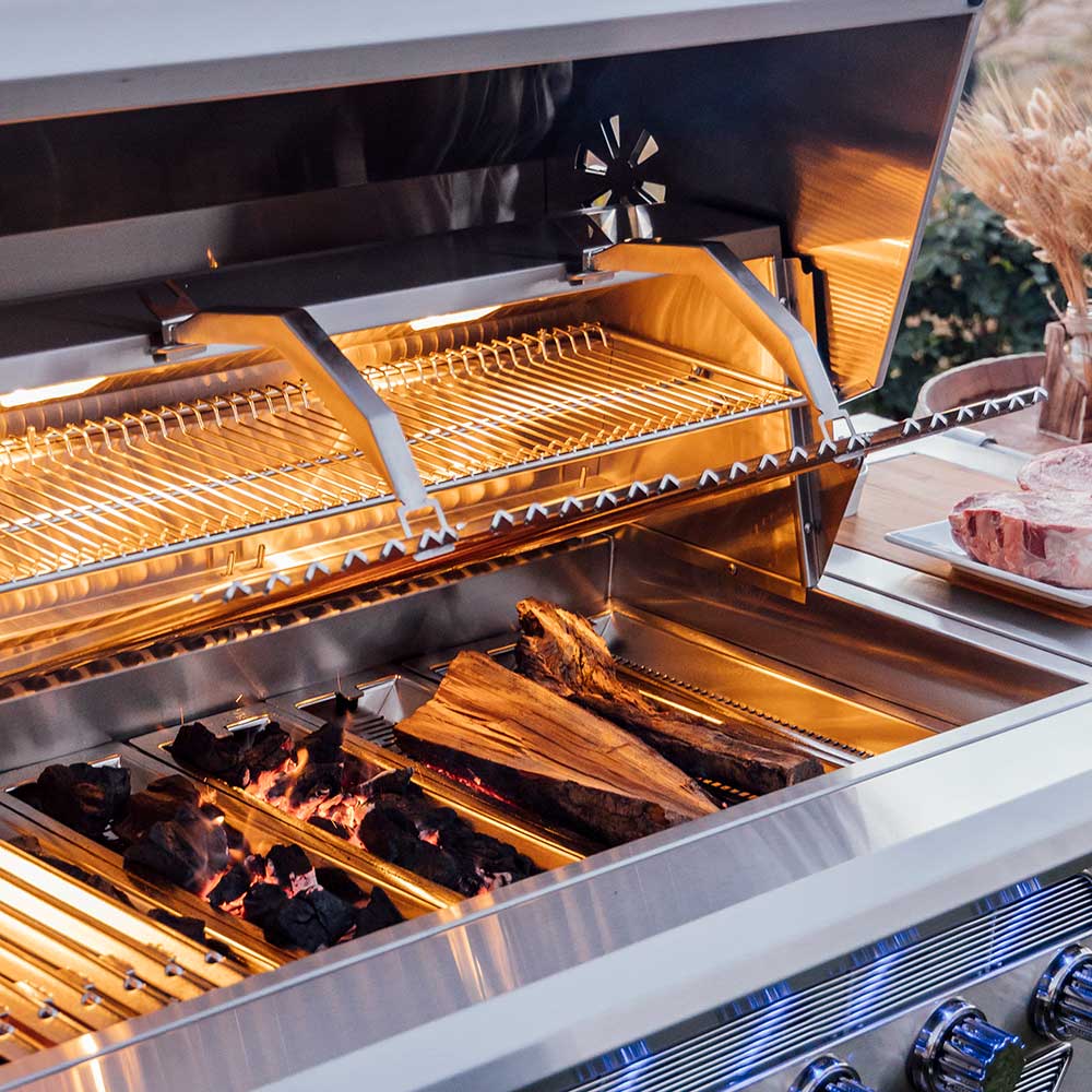 Dual fuel grill with wood logs and glowing coals under open hood grates