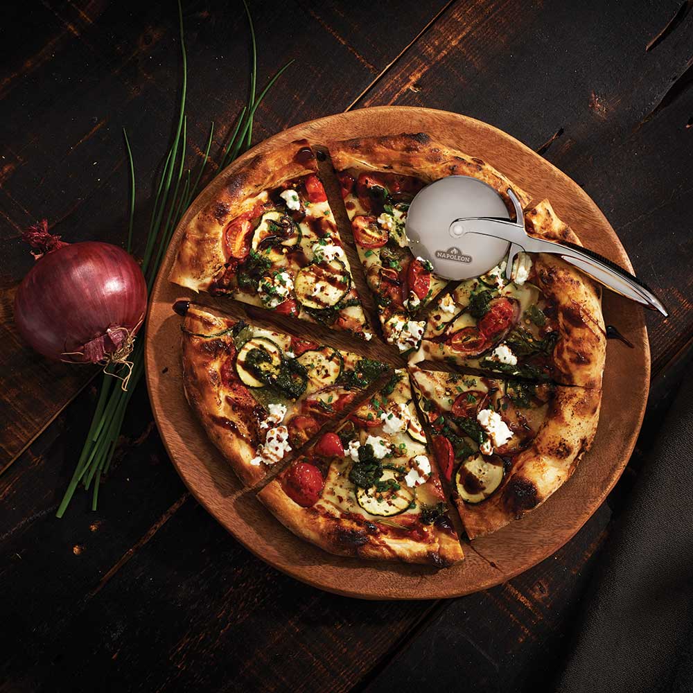 Stainless pizza wheel resting on sliced vegetable pizza