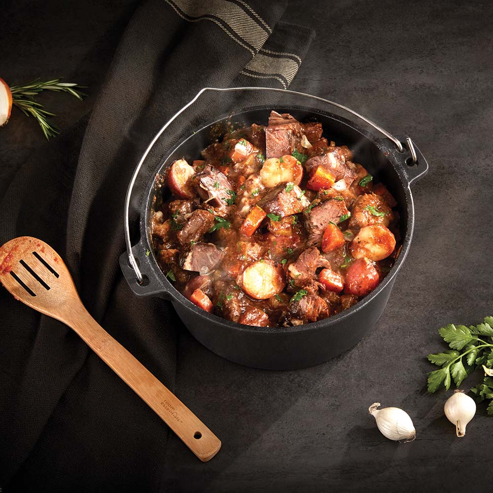 Cast iron Dutch oven filled with browned stew and vegetables, topped with herbs