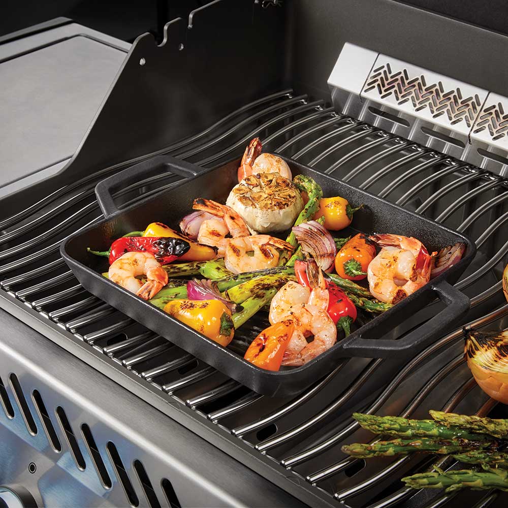 Square cast iron griddle cooking shrimp and vegetables on ridged grill surface