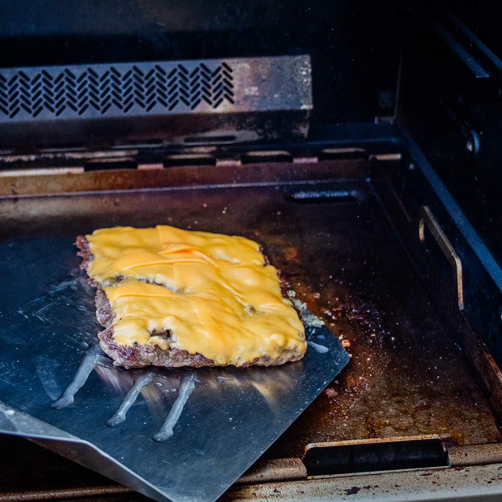 Rectangular metal griddle insert with a cheeseburger cooking on the plate