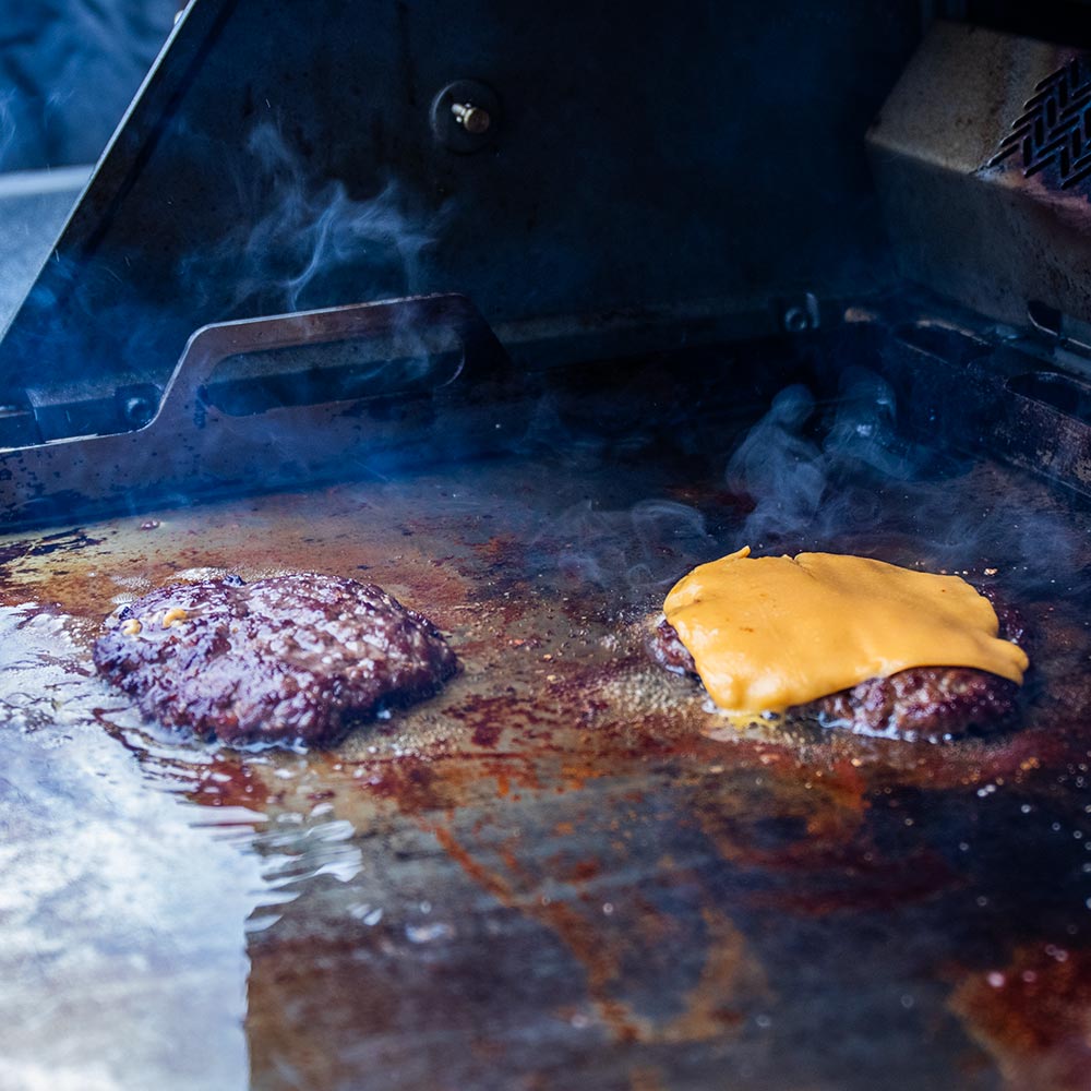 Rectangular metal griddle insert with side handles, heating food over an open grill