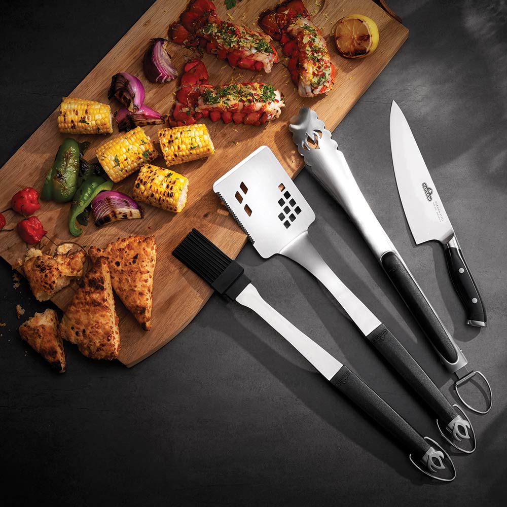 BBQ tool set with black handles: spatula, tongs, fork, and knife on board.