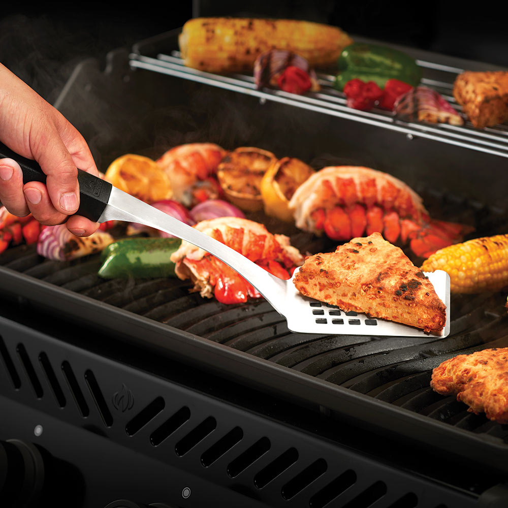 Stainless steel spatula with black handle lifting grilled seafood and vegetables.