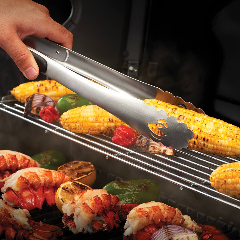 BBQ tongs with black grip holding roasted corn over a grill.