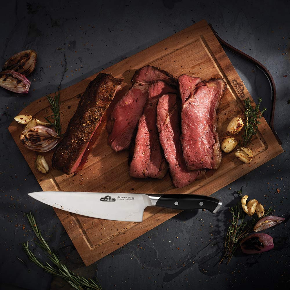 Wood cutting board with chef knife and sliced meat arranged in center.