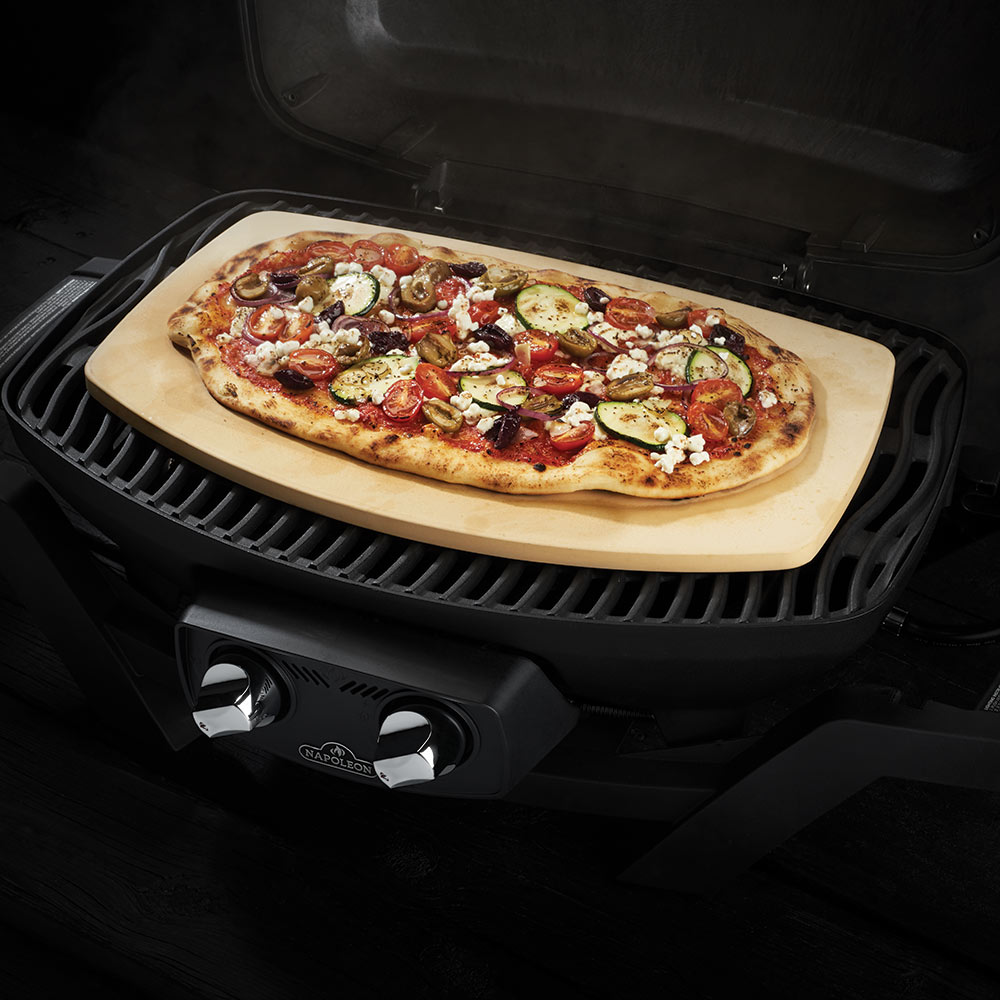 Pizza stone in grill with a topped pizza on a light tan baking surface