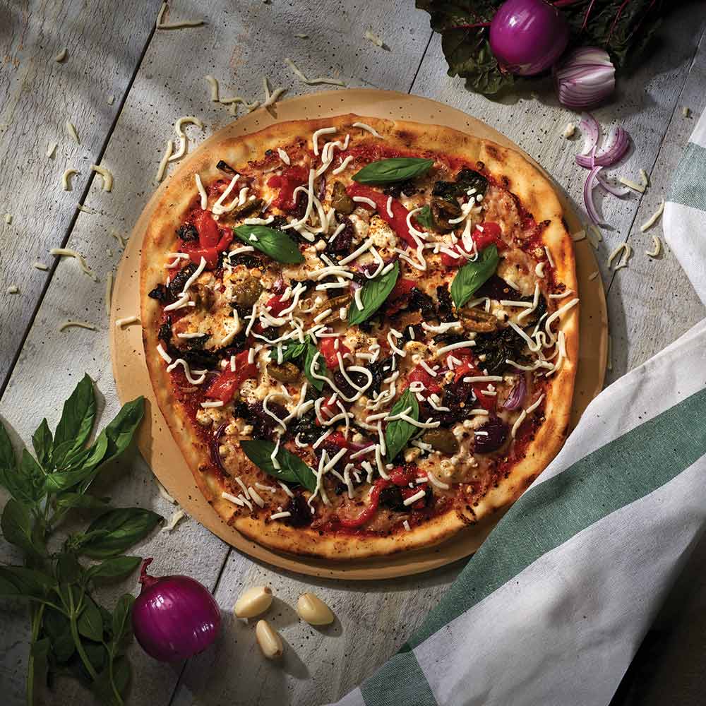 Round pizza on a tan pizza stone, topped with vegetables and cheese