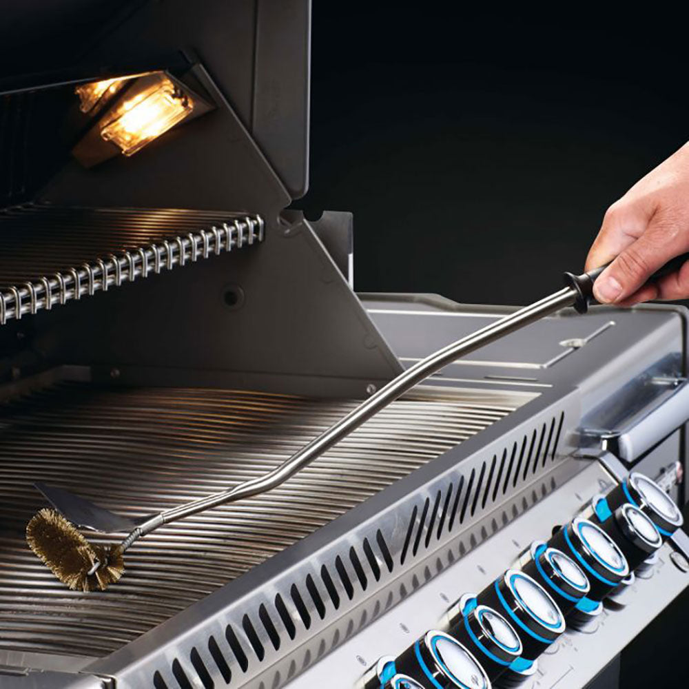 Grill grid brush with long handle on cooking grates, near an LED light