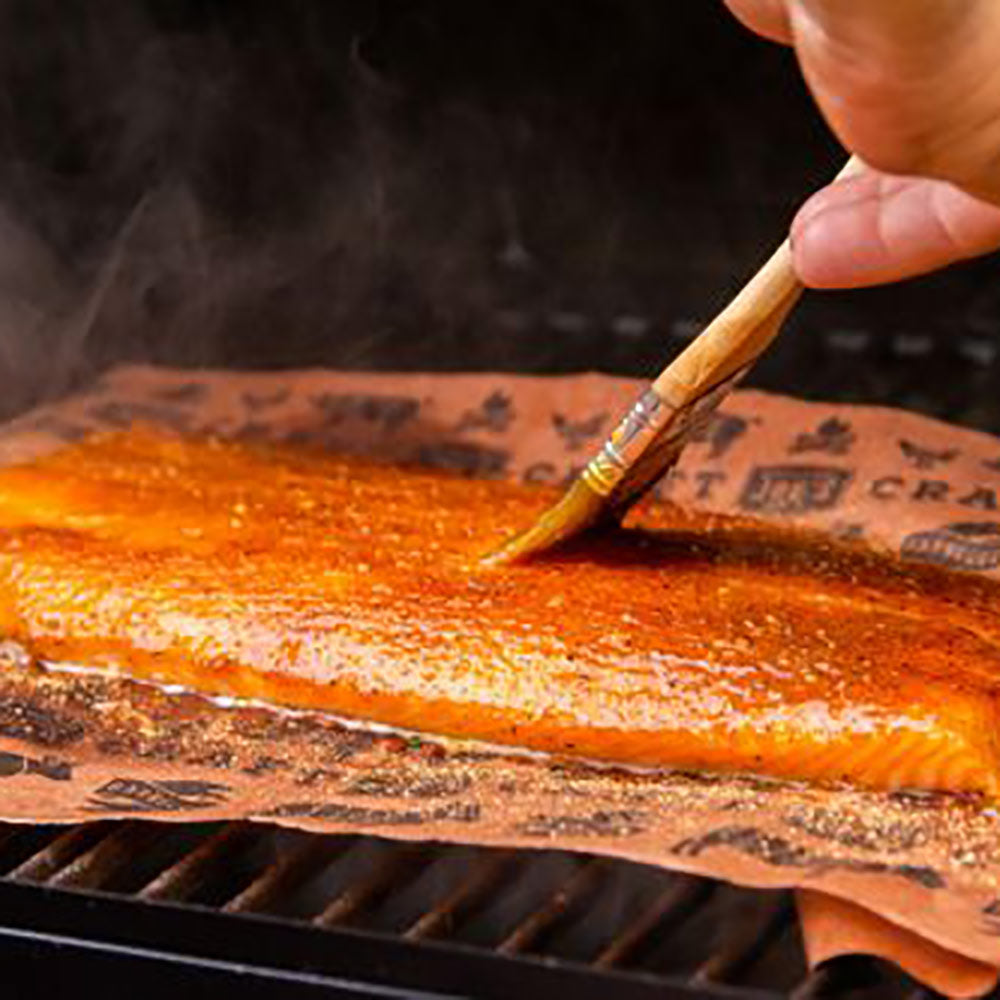 Printed peach butcher paper on a grill with sauce brushed over the meat