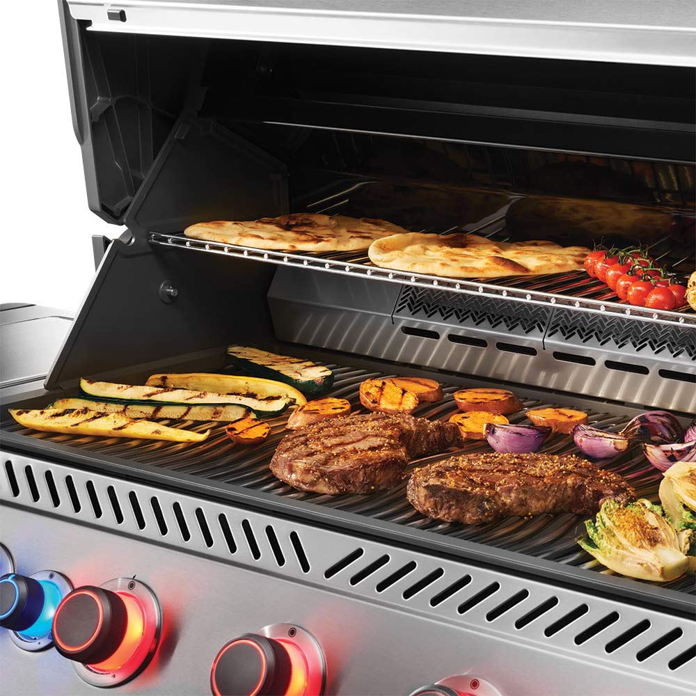 Gas grill with open lid showing cooking grates filled with burgers and sliced vegetables