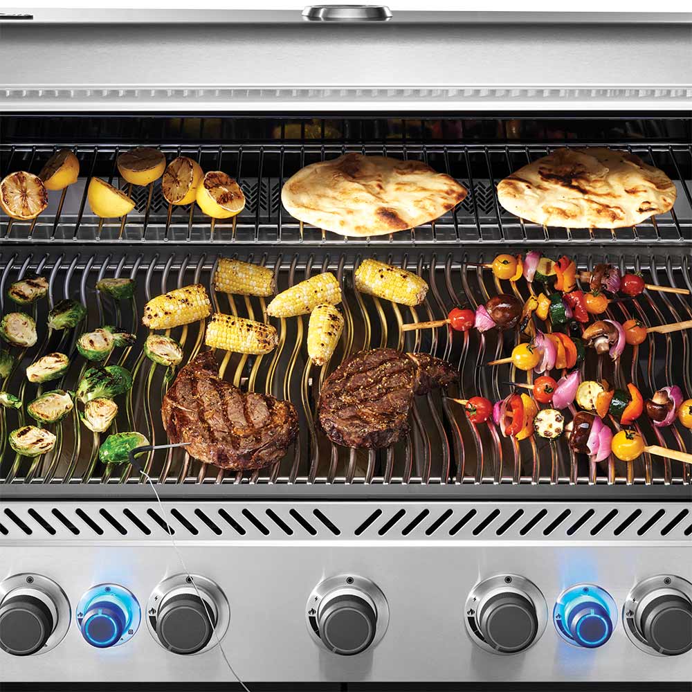 Gas grill cooking surface with meats, corn, vegetables, and knobs along the front panel