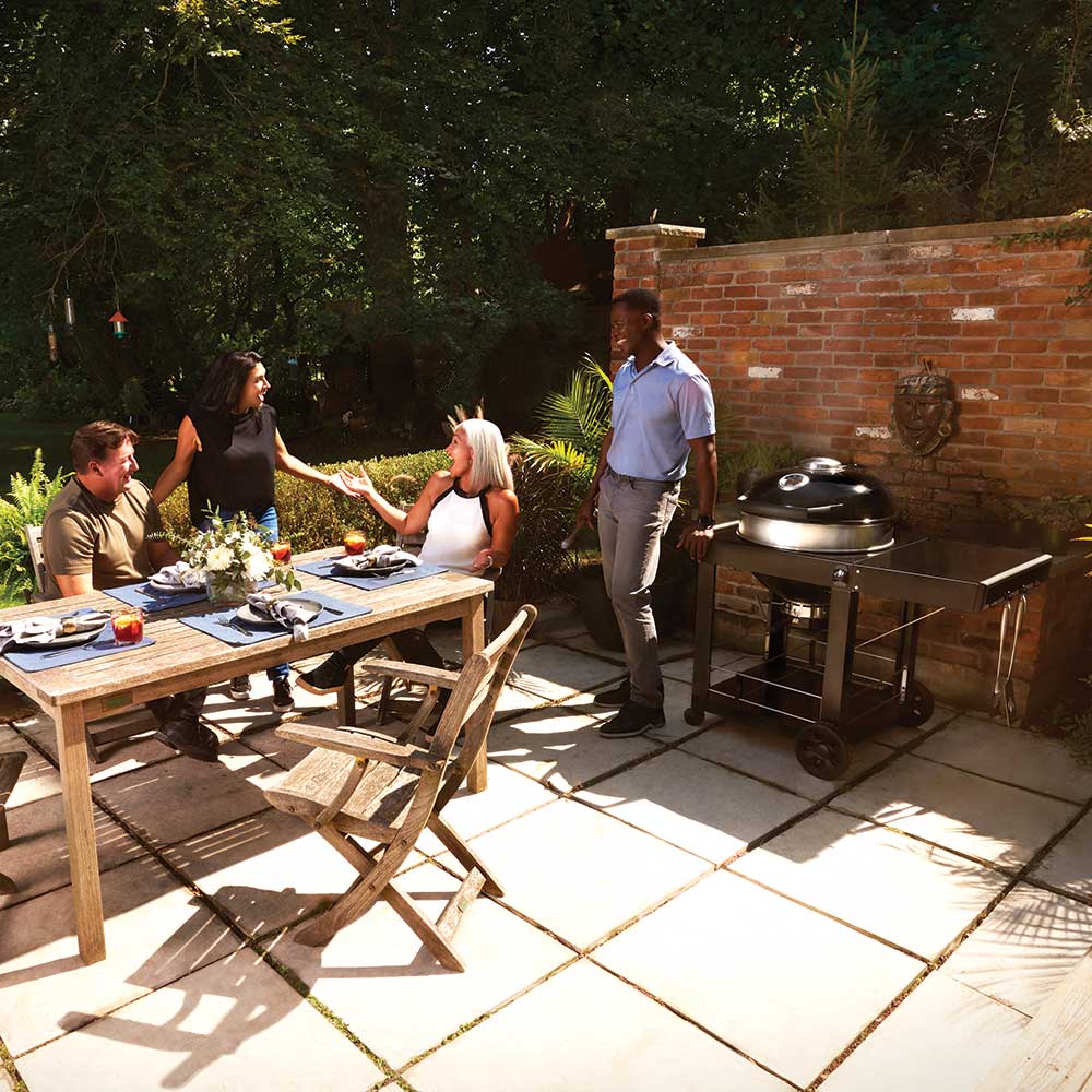 Charcoal kettle grill with cart and side table on a patio, ready to cook