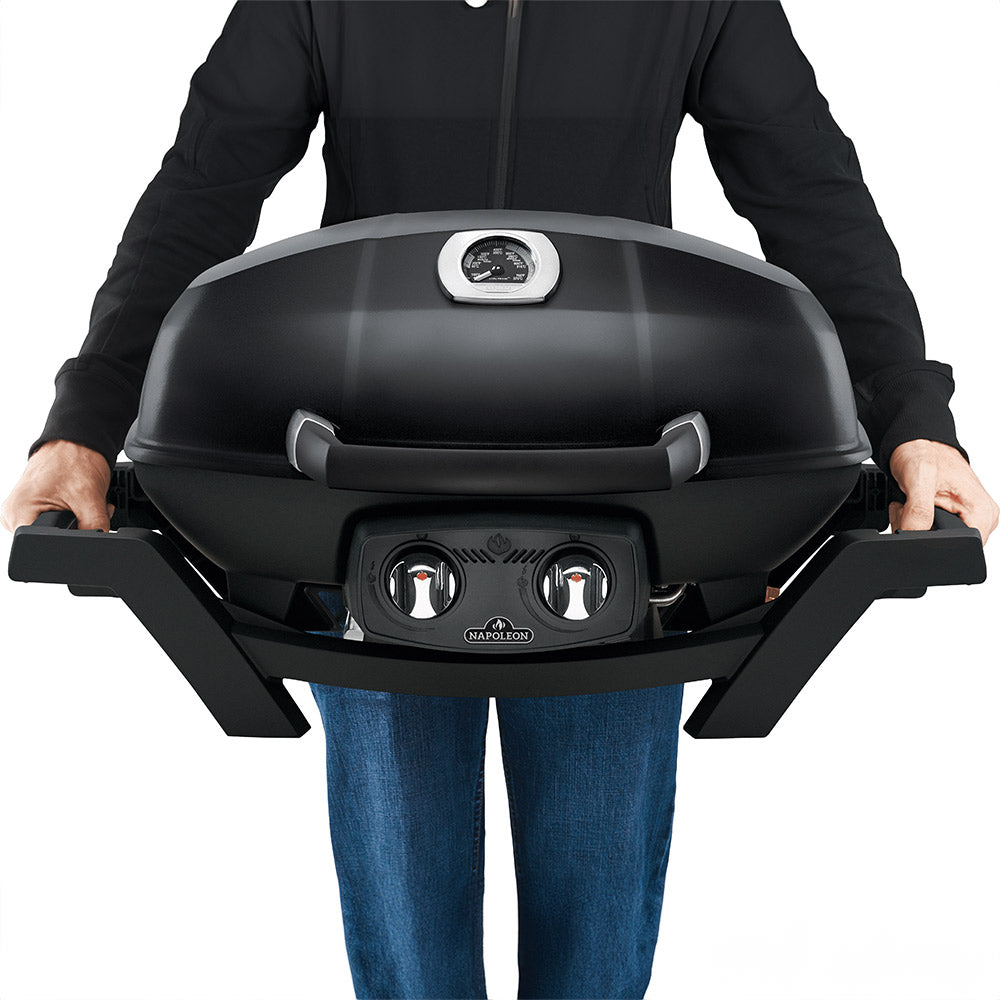 Black portable tabletop gas grill held by person, showing domed lid handle and control knobs