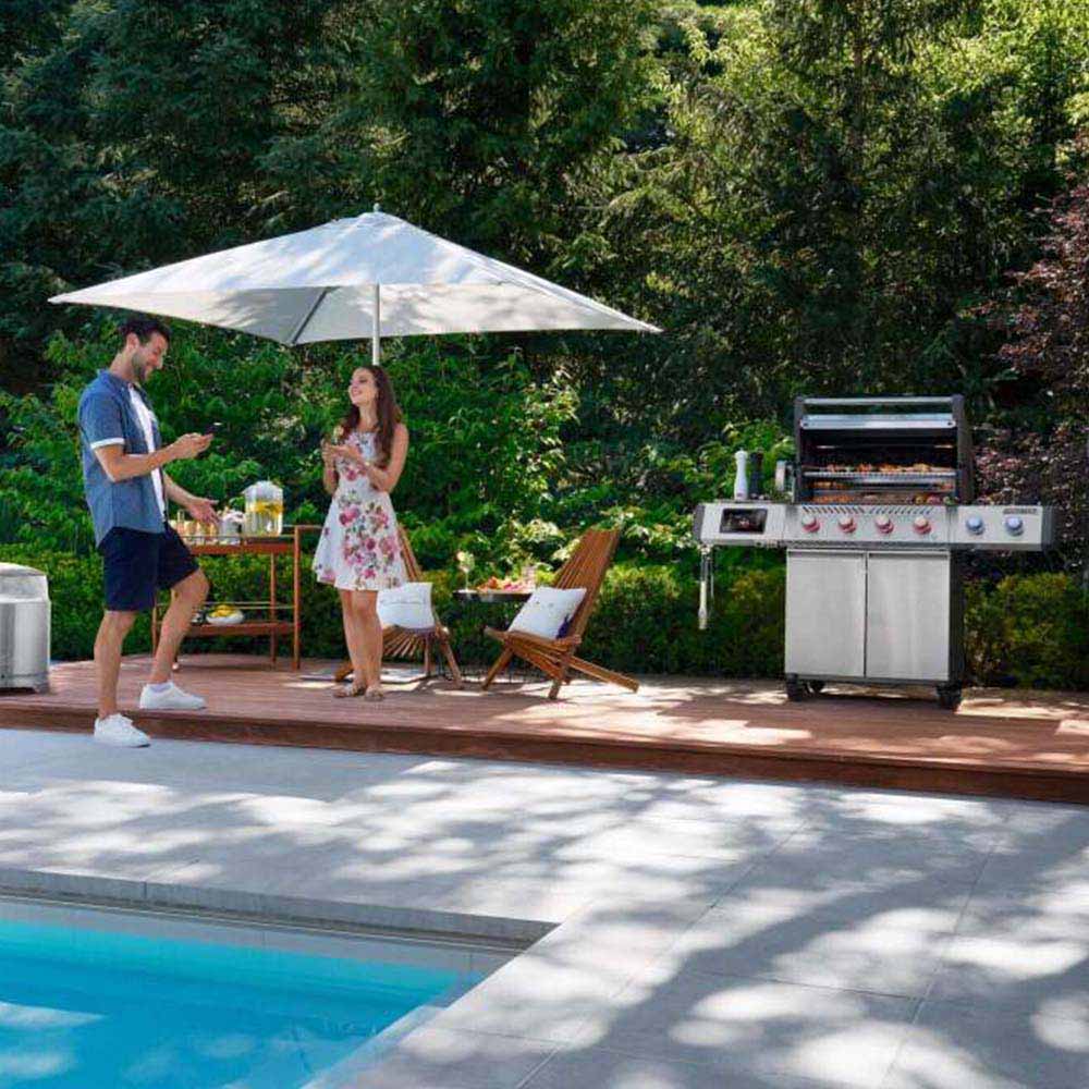 Stainless steel gas grill with closed hood, front knobs, and side shelf on patio