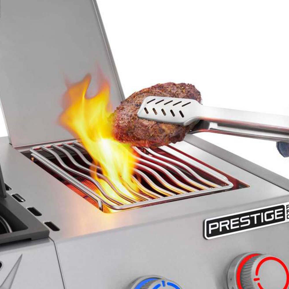 Gas grill burner with visible flames under a searing grate near a cooking burger