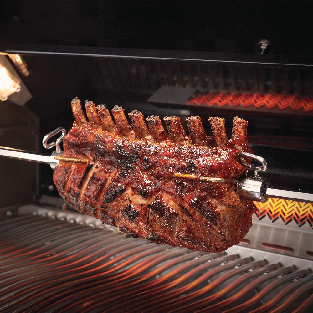 Rotisserie roasted meat on spit in gas grill with glowing heating elements