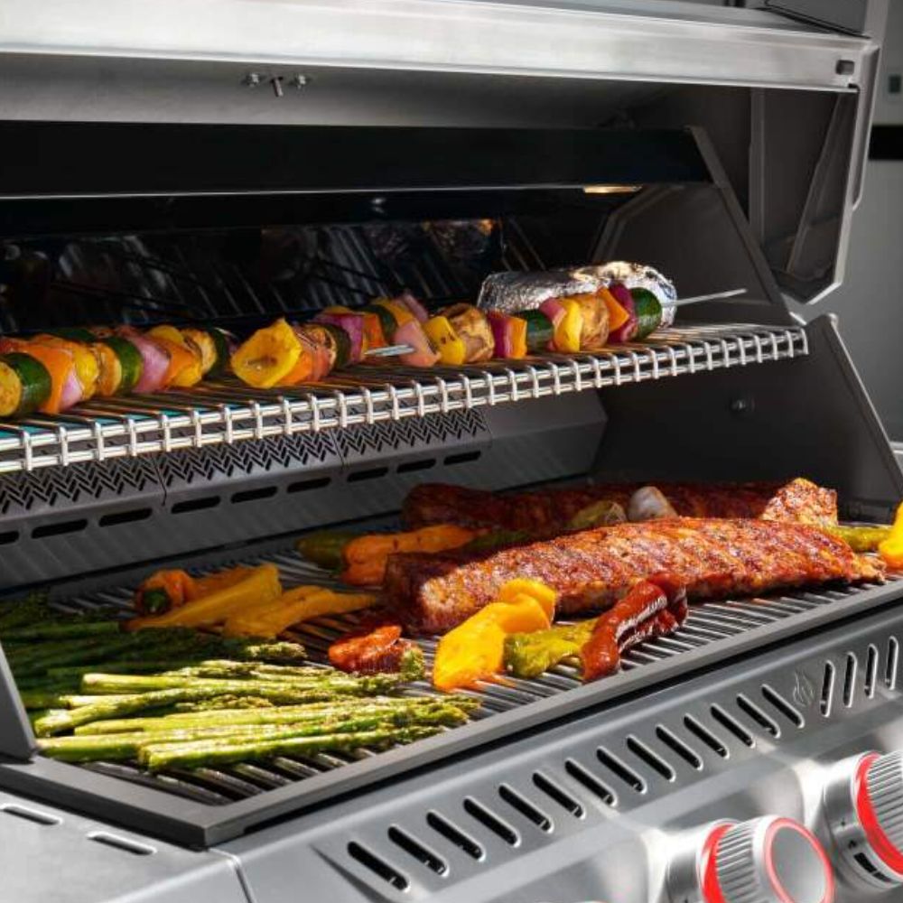 Open gas grill lid showing cooking grates with colorful food and glowing burner flame