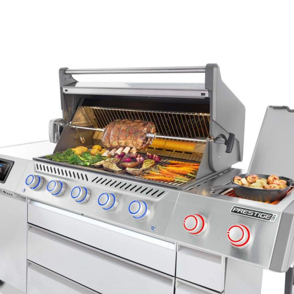 Open gas grill with rotisserie-style tray and food on the cooking grate