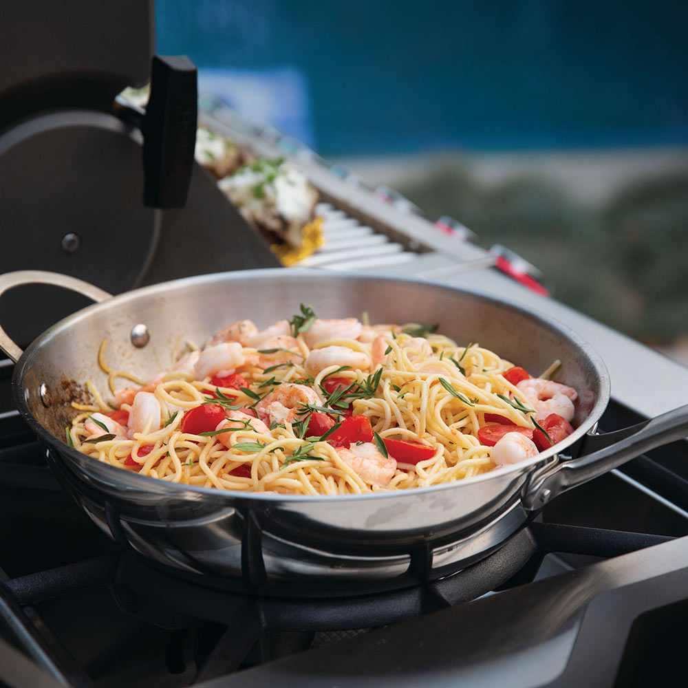 Stainless steel grill pan with spaghetti and vegetables on burner grates
