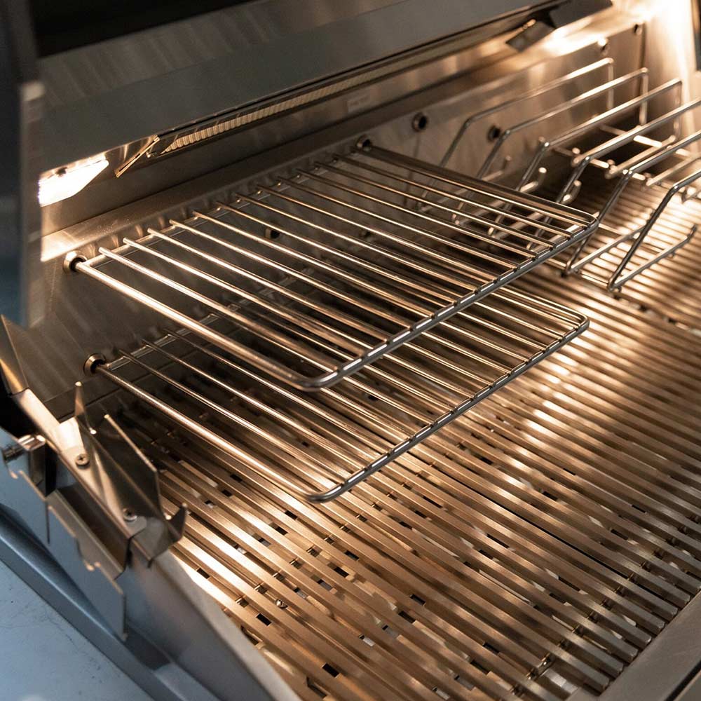 Stainless steel cooking grates with warming rack inside illuminated grill hood.