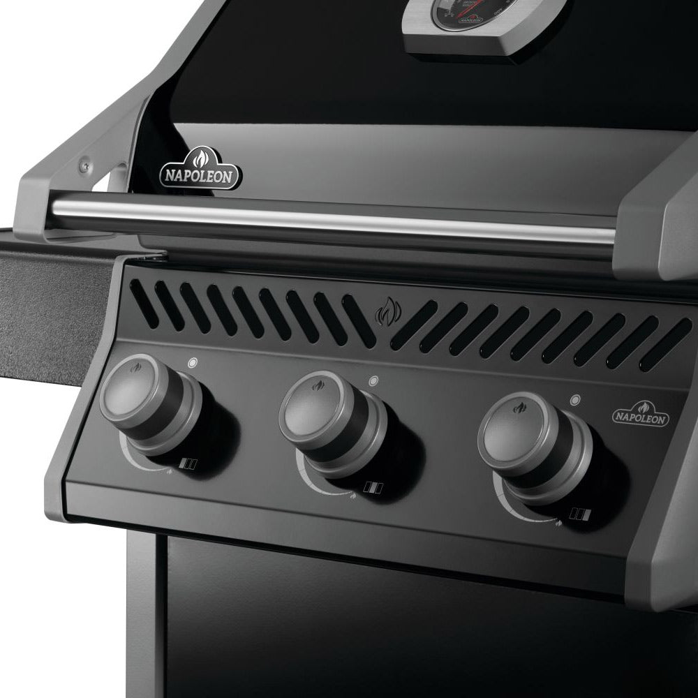 Gas grill burner area with three gray knobs and vented heat shield