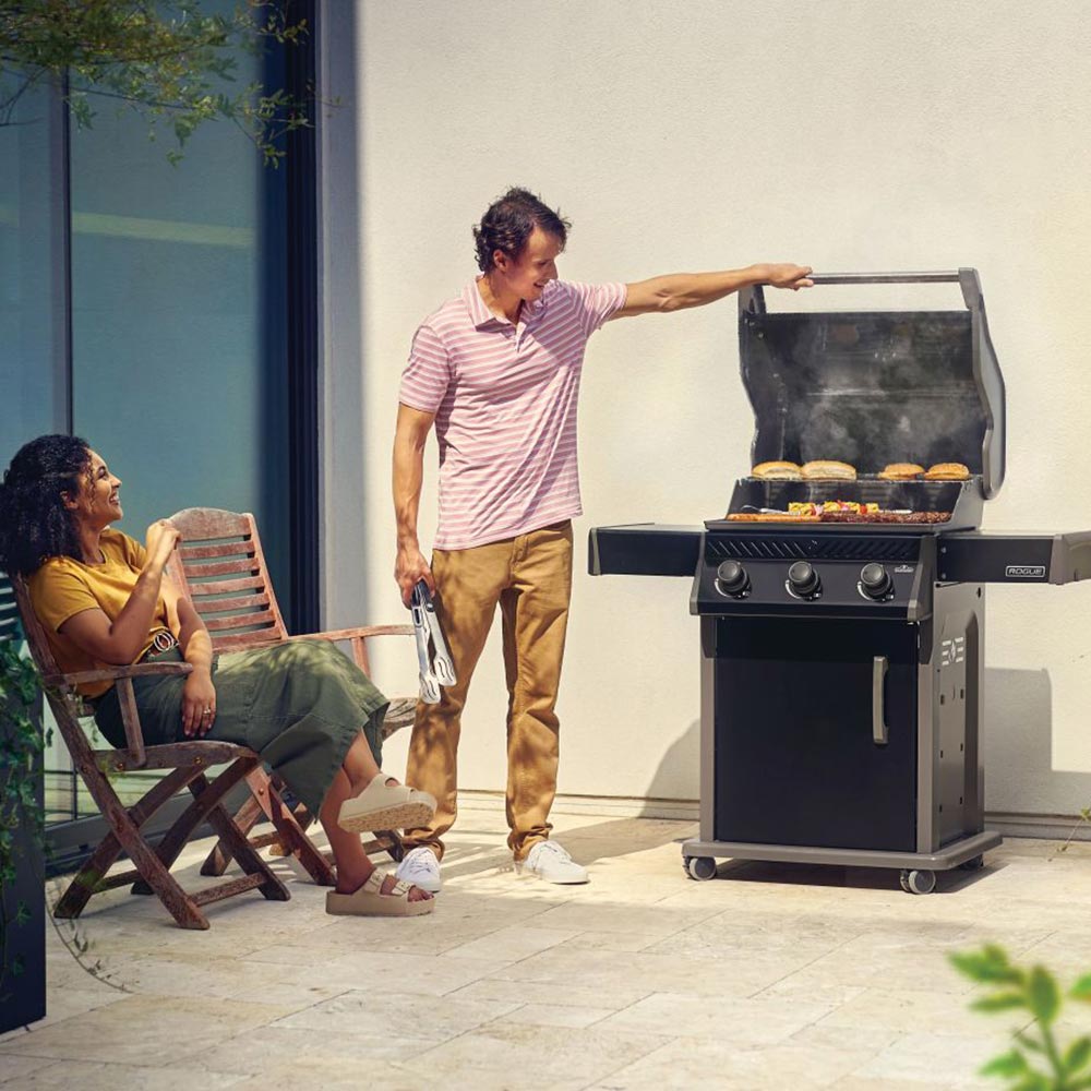 Gas grill on cart in outdoor patio with lid open and food on the grates