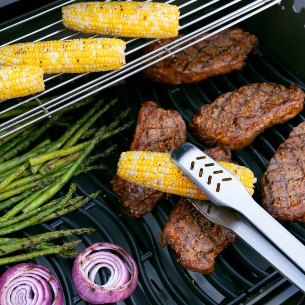 Gas grill cooking grate with corn, asparagus, and grilled meat and spatula