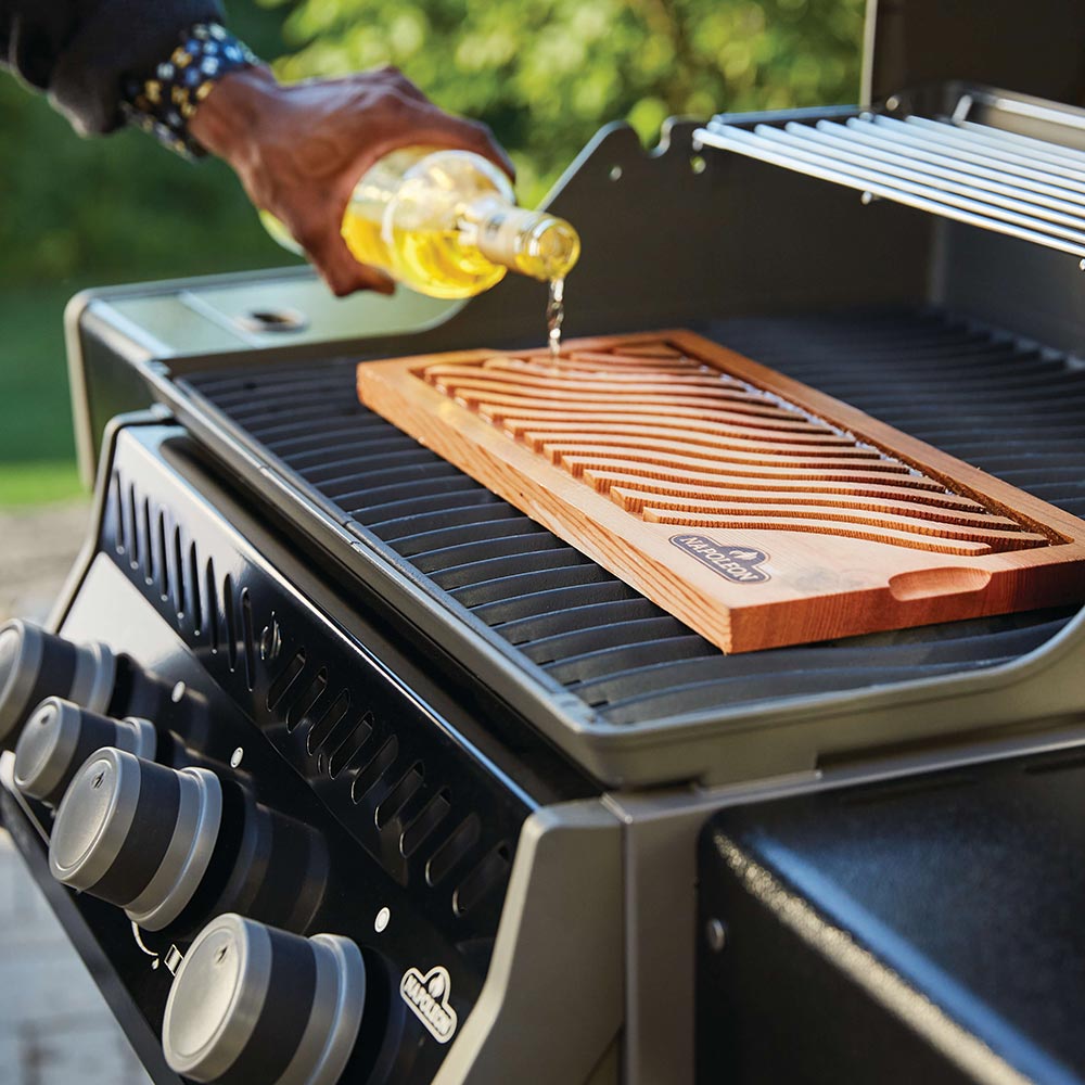 Gas grill grates with wooden plank and oil being poured from a bottle
