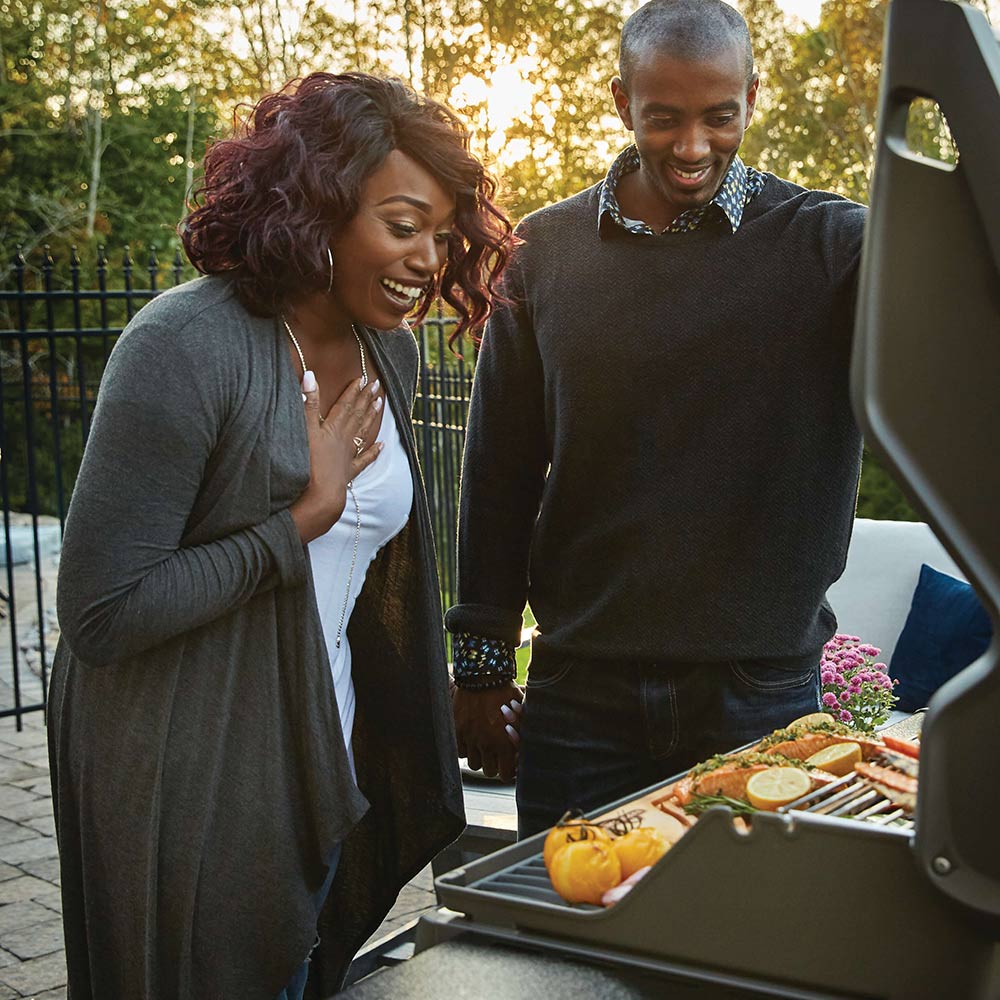 Black gas grill on cart with open lid and food on the cooking surface