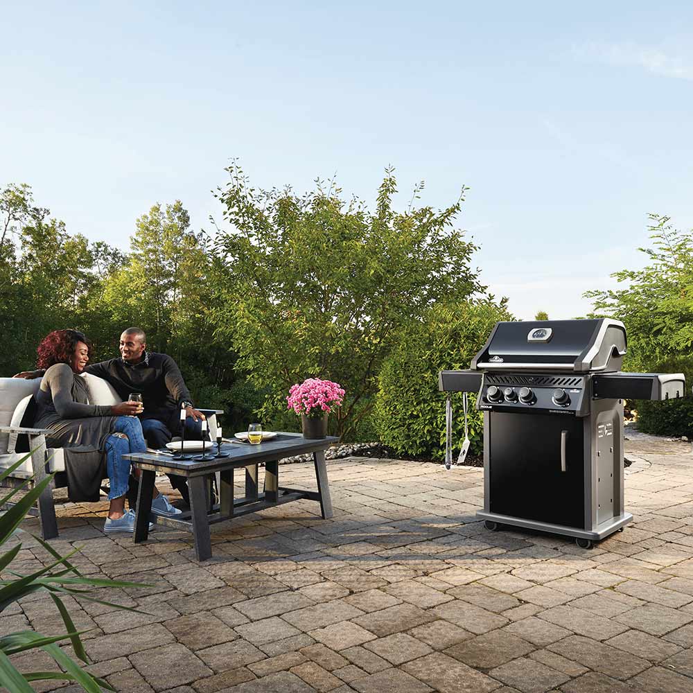 Black gas grill on cart outdoors, front controls and side shelves visible