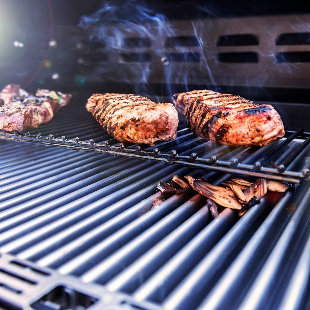 Grilled steaks on black grates inside infrared grill with visible smoke