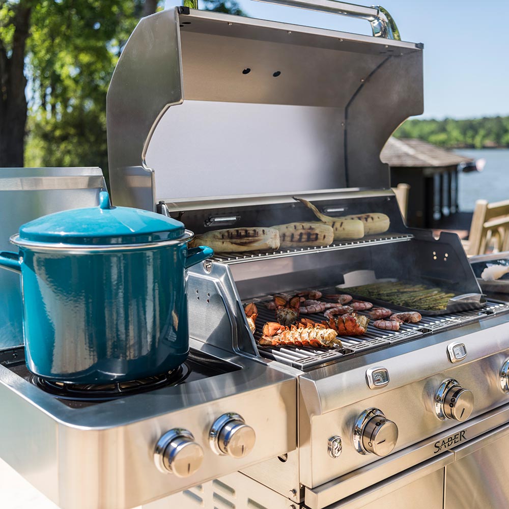 Stainless steel infrared grill with lid open, side burner, and food on warming/side surface