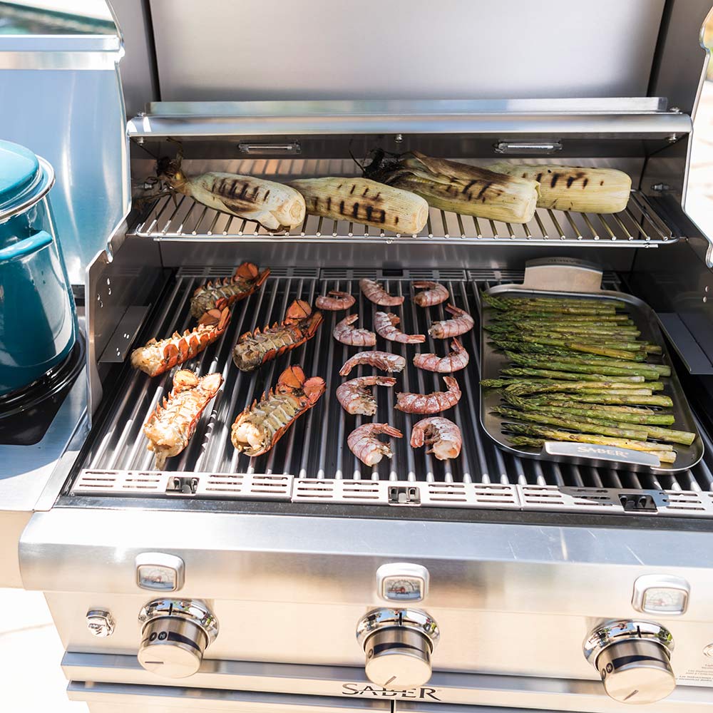 Infrared grill interior with shrimp, vegetables, and sausages on cooking grates