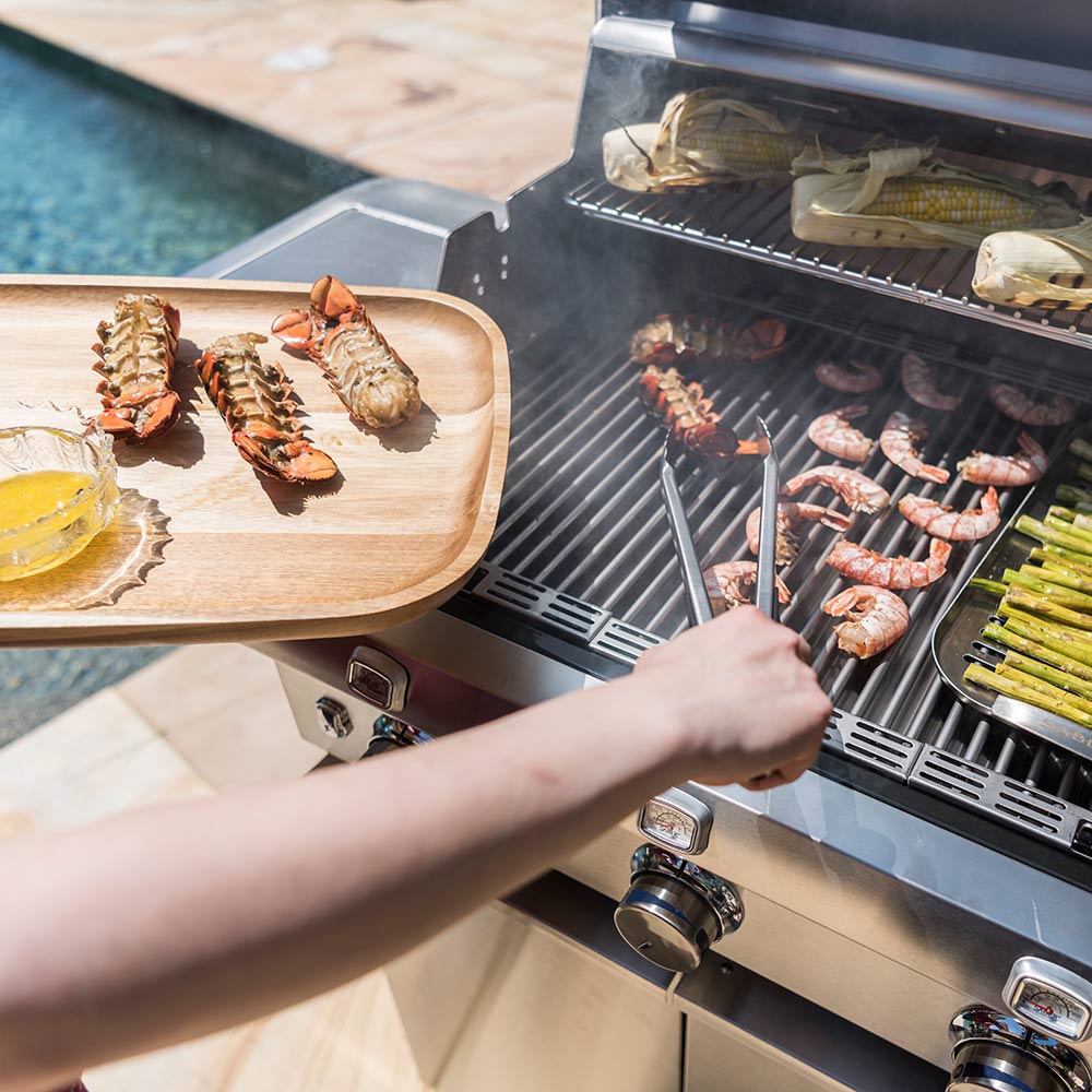 Hand grilling food on an open stainless steel infrared grill with sausages and asparagus