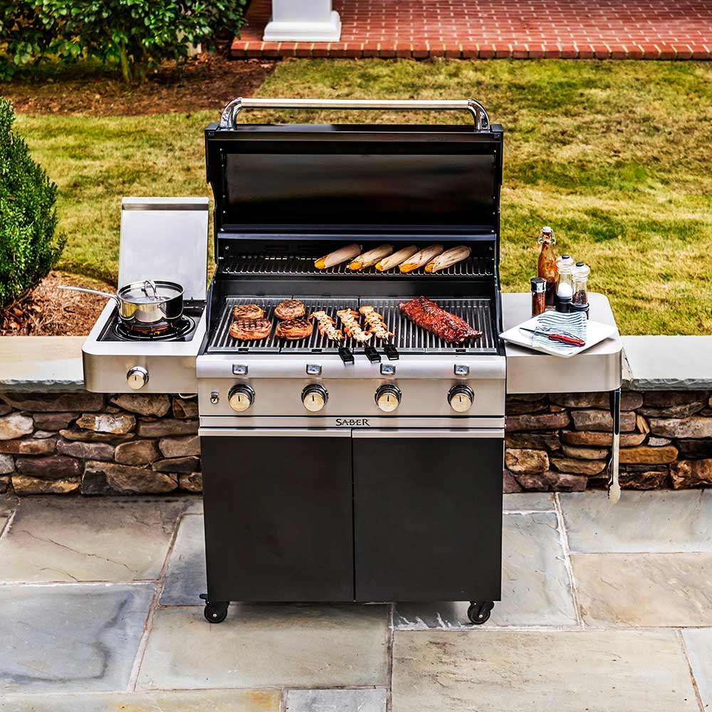 Infrared grill outdoors with lid open, grilling food on grates and side burner shelf