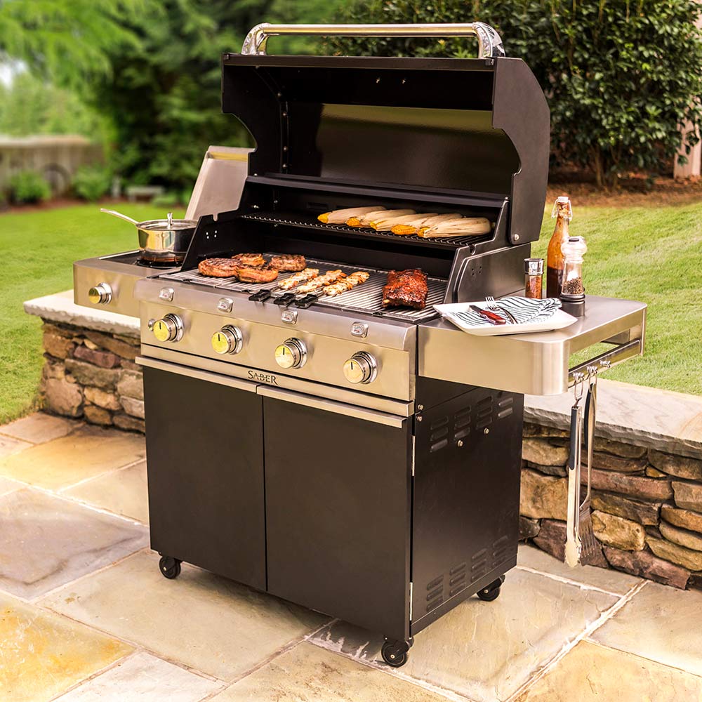 Infrared grill with open lid and grilling food on grates, black cabinet and side shelves