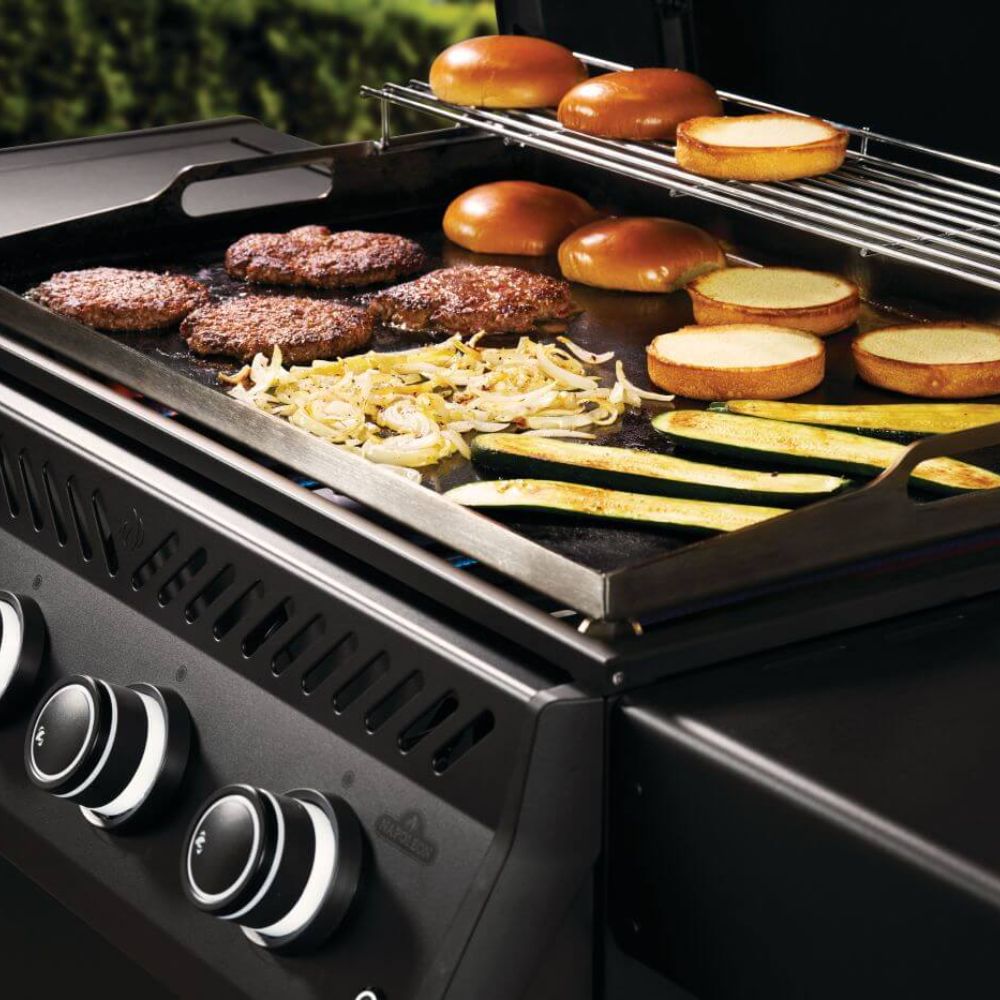 Gas griddle cooking surface with burgers, sliced vegetables, and burner grates