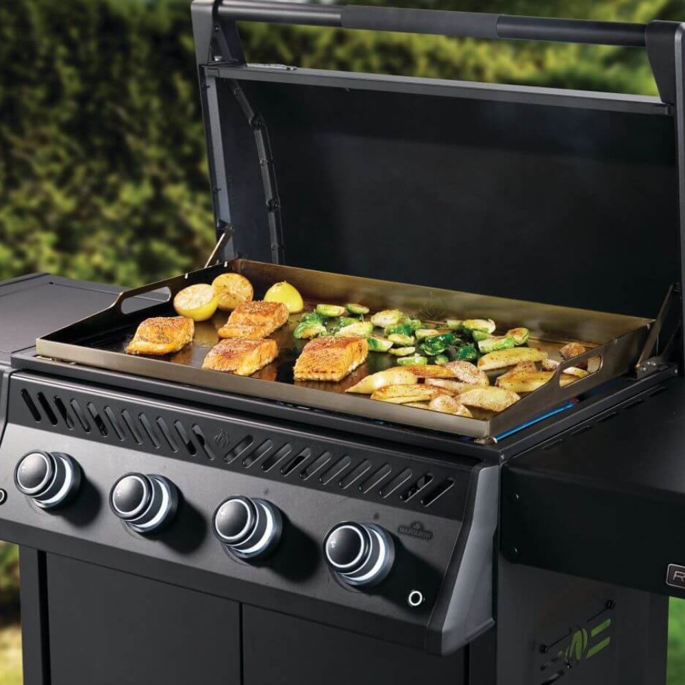 Black gas griddle grill with lid open and food cooking on metal grates