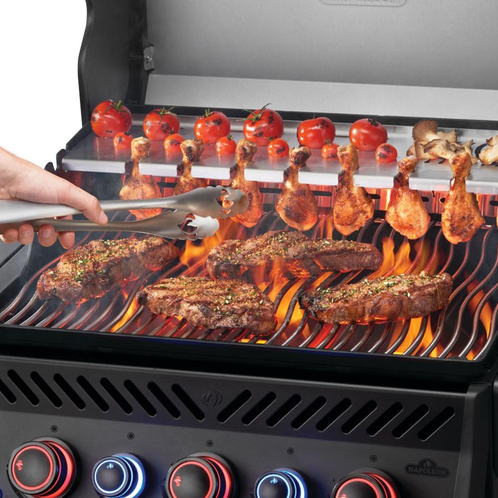 Gas grill cooking grates with kebabs and chicken as flames rise, lid open