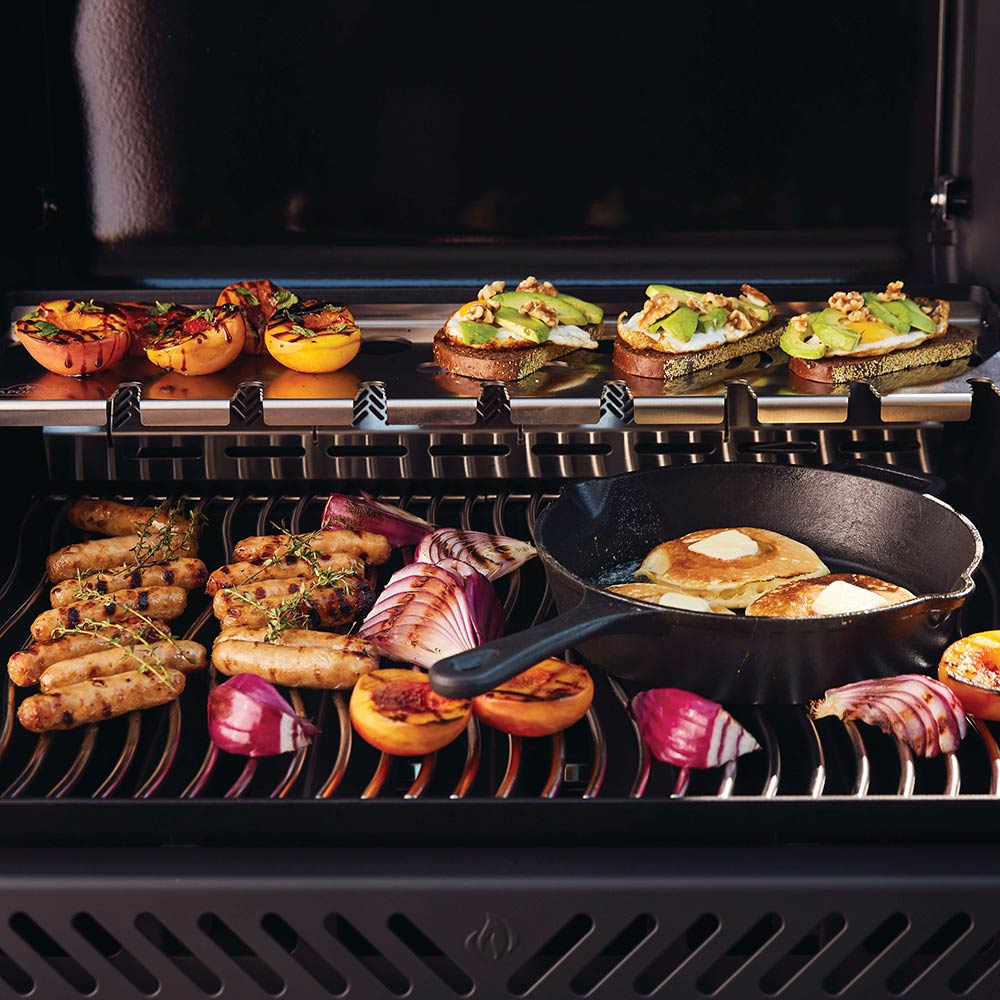 Gas grill cooking grates with burgers and vegetables inside open hood