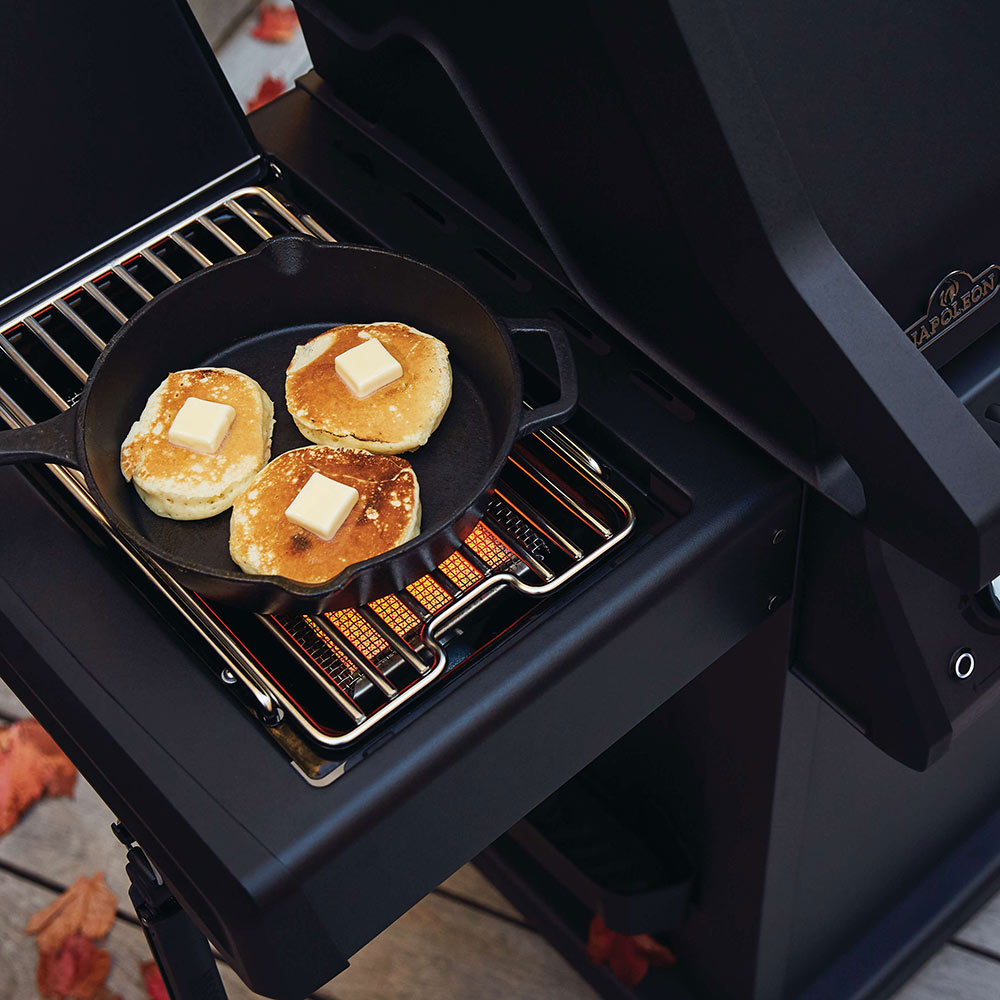 Side burner skillet on black gas grill with bread and toppings cooking