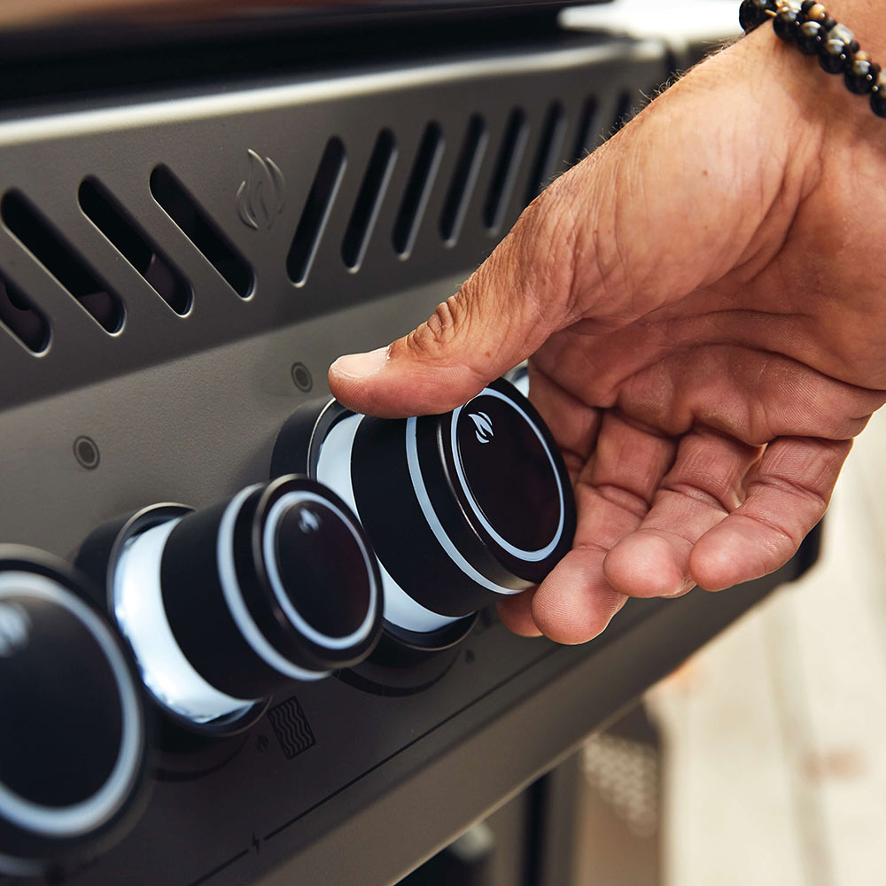 Hand adjusting black gas grill control knobs on front panel