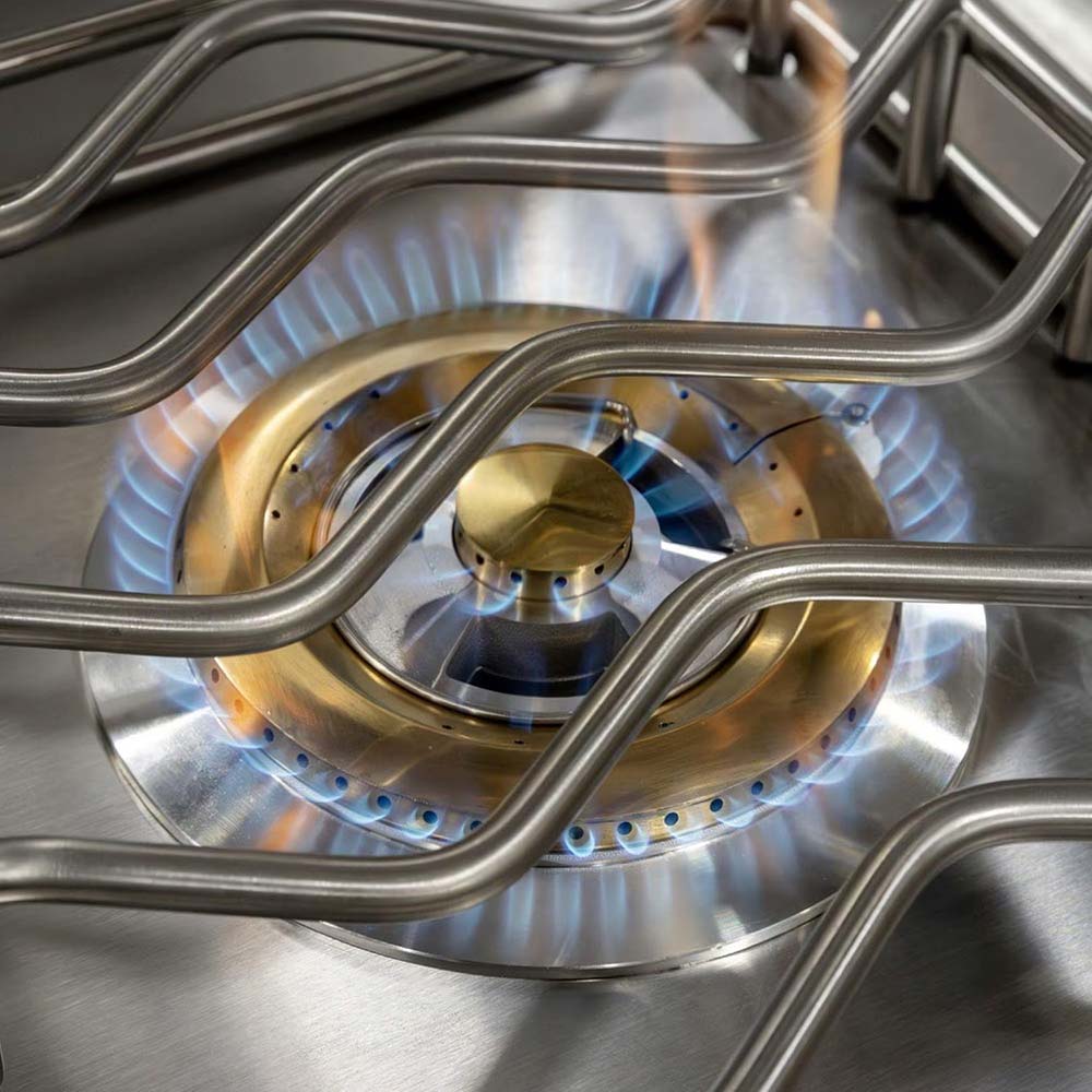 Built-in side burner with brass burner head and blue flame under grates
