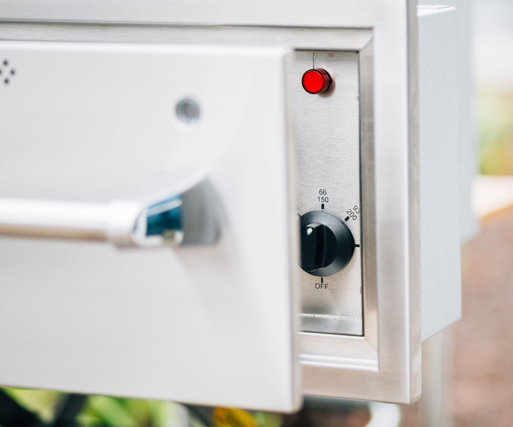 Warming drawer control panel with red indicator light and temperature dial.