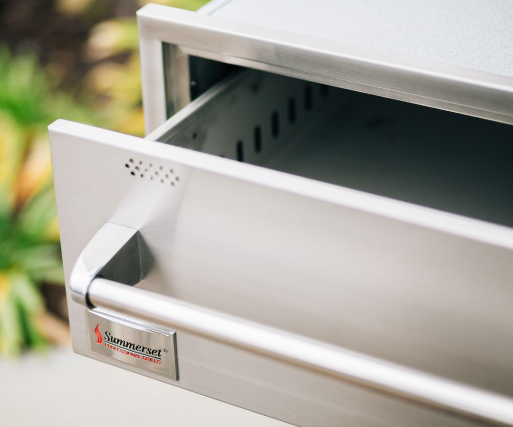 Stainless steel warming drawer door open, showing interior and control label.