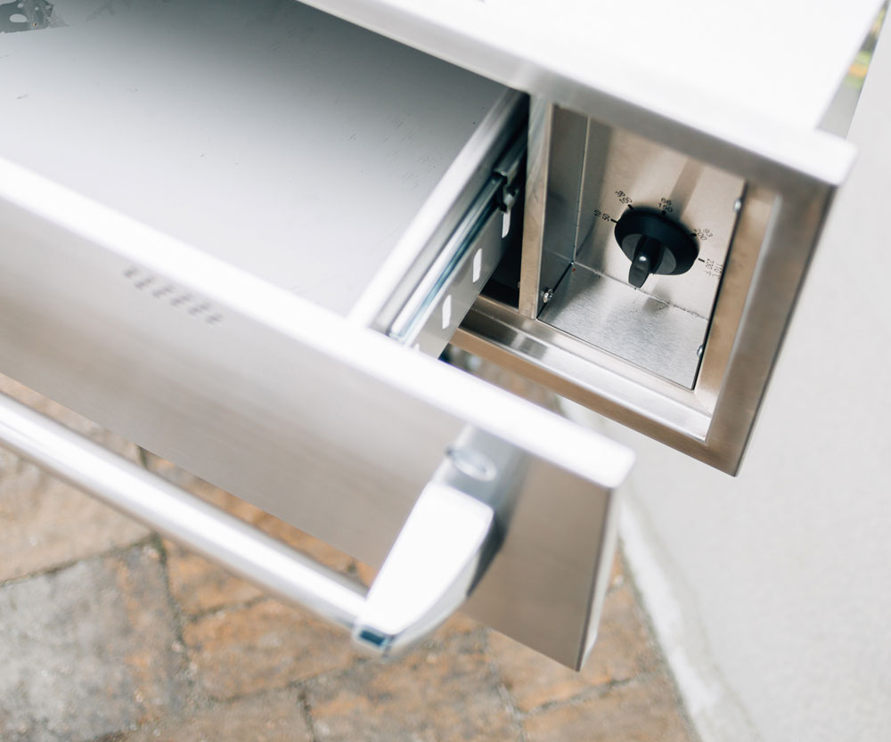 Open stainless steel warming drawer, showing interior components and temperature knob.