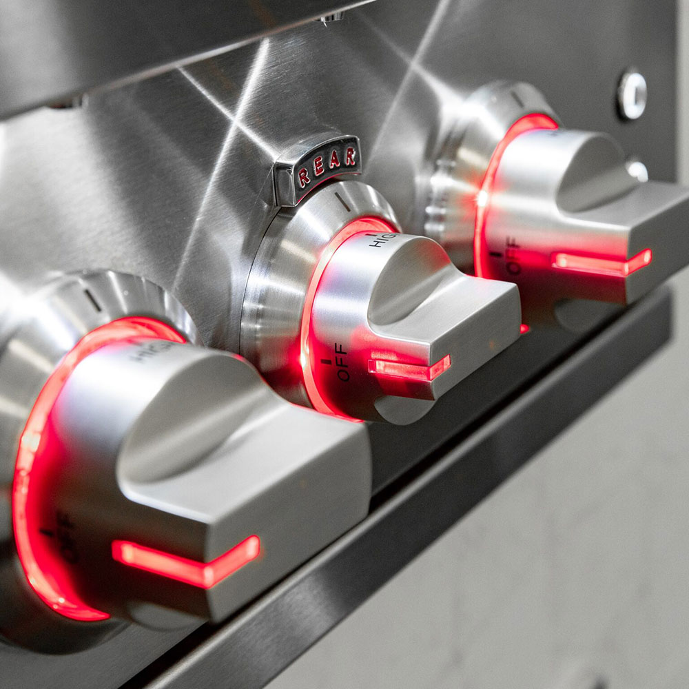 Stainless gas grill control panel with knobs and red flame indicators