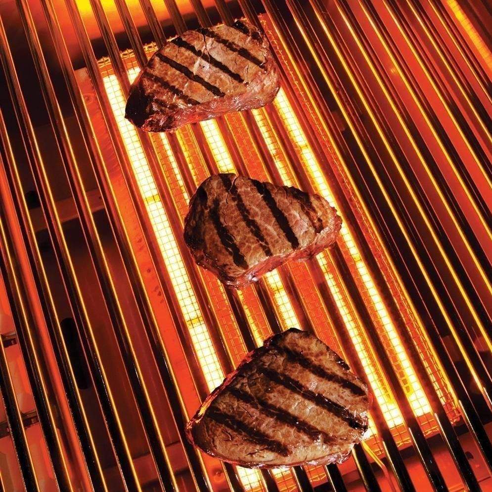Grilled steaks on open gas grill grates over glowing burner tubes.